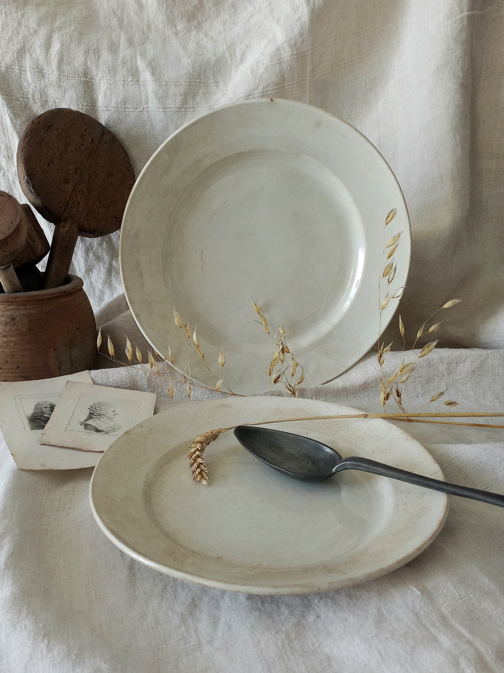 Two antique plates on a textured surface with a spoon and wooden items.
