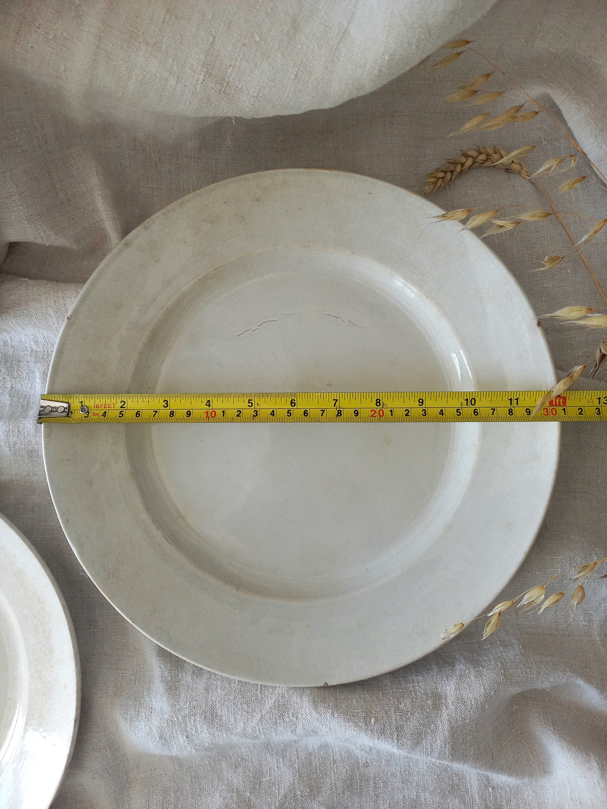 Antique white plate with a measuring tape indicating its diameter on a textured surface.