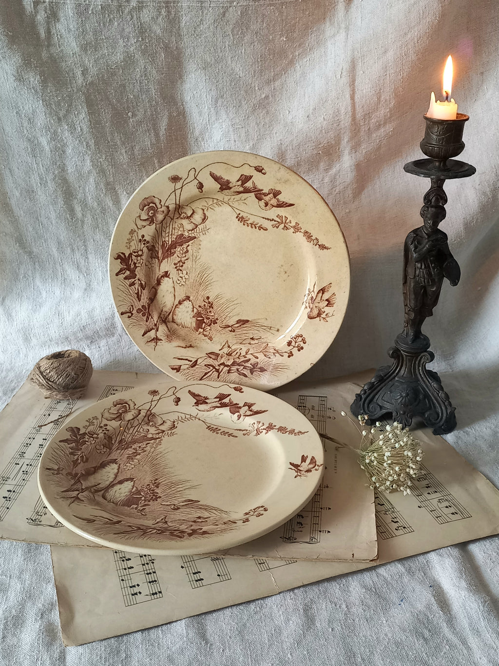 Two decorative antique plates with intricate floral and bird designs on a surface with a candle and paper.