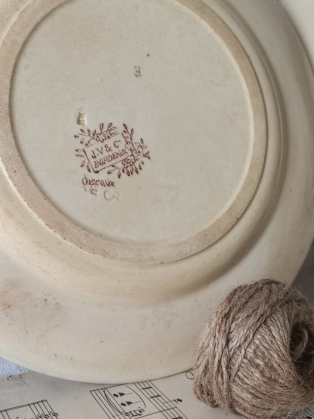 Ceramic plate with a decorative logo and text, next to a ball of twine on a surface with music sheet.
