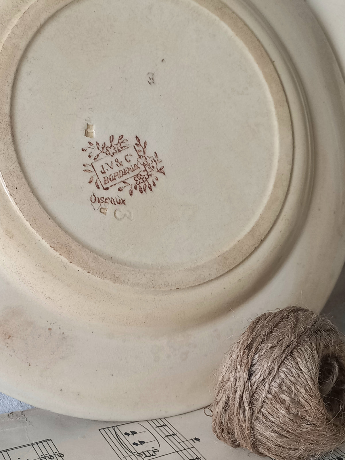 Ceramic plate with a decorative logo and text, next to a ball of twine on a surface with music sheet.
