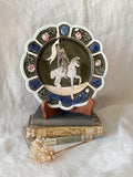 Decorative plate with a scene of Joan of Arc on a horse, surrounded by decorative elements on a white background.