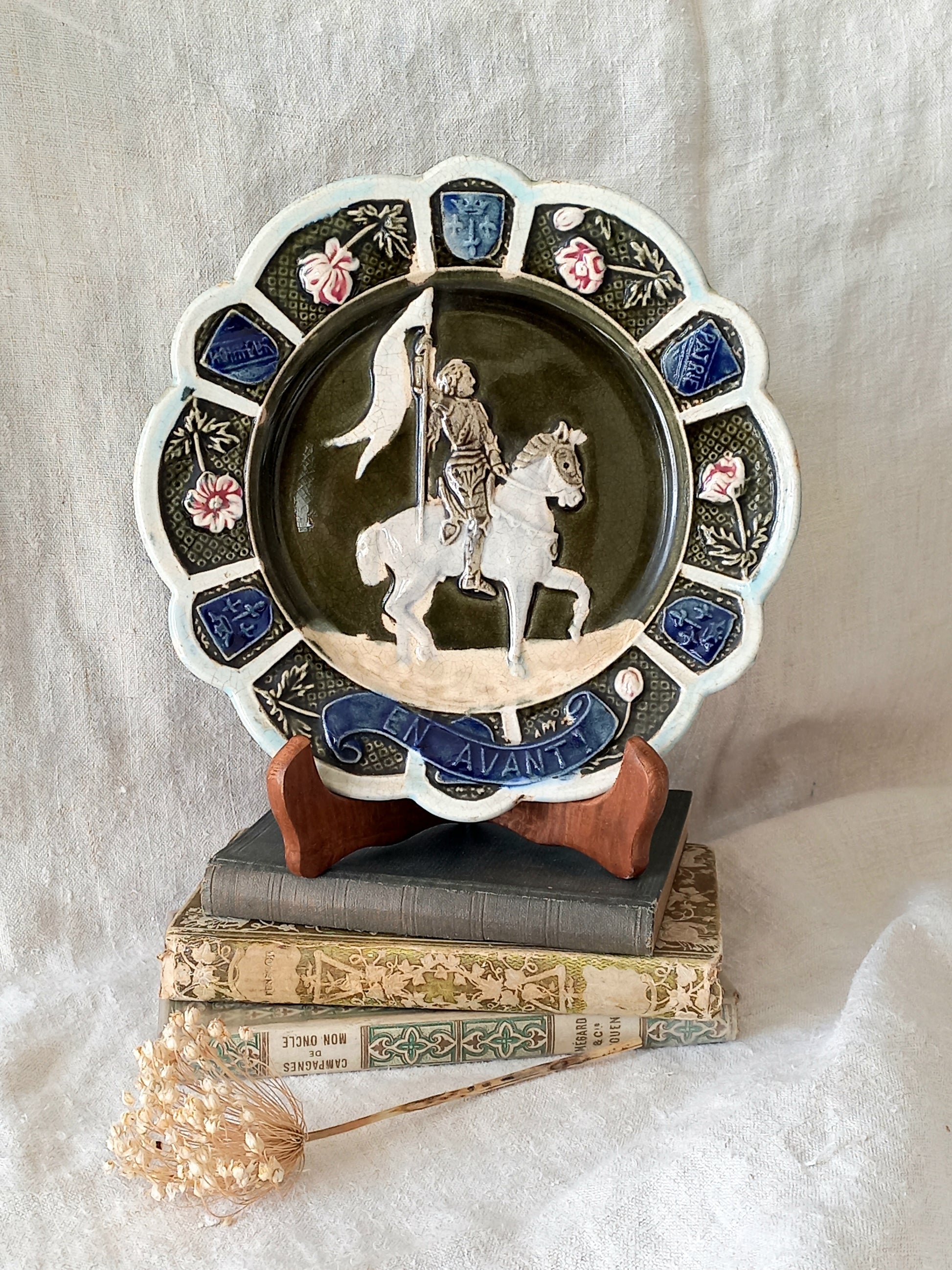 Decorative plate with a scene of Joan of Arc on a horse, surrounded by decorative elements on a white background.