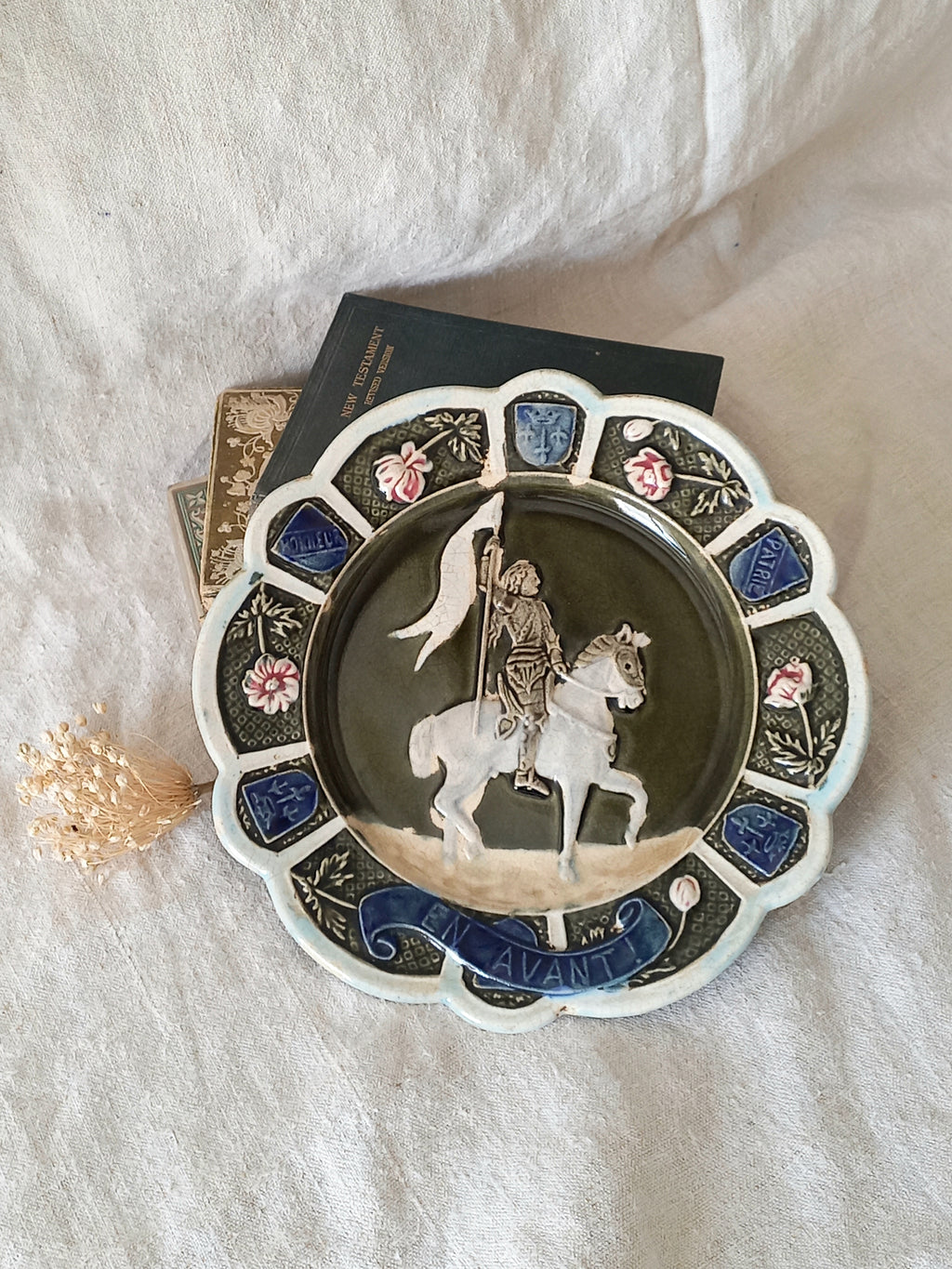 Decorative plate with a scene of Joan of Arc on a horse, surrounded by decorative elements on a white background.