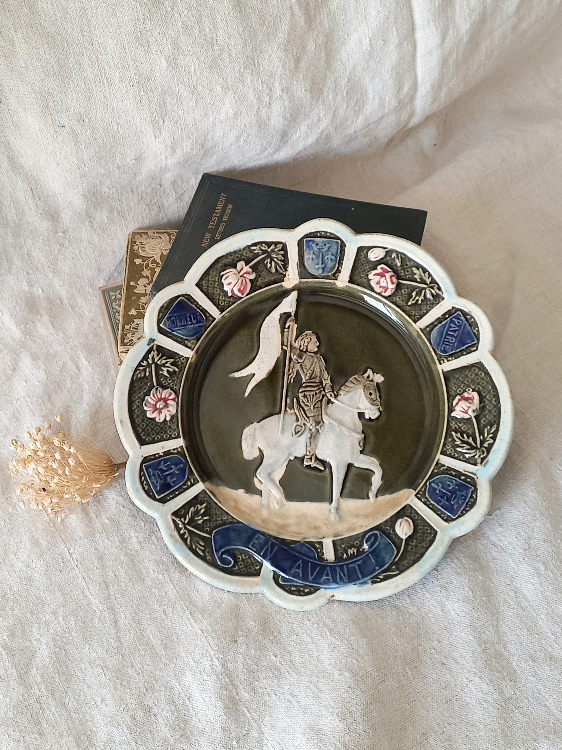 Decorative plate with a scene of Joan of Arc on a horse, surrounded by decorative elements on a white background.