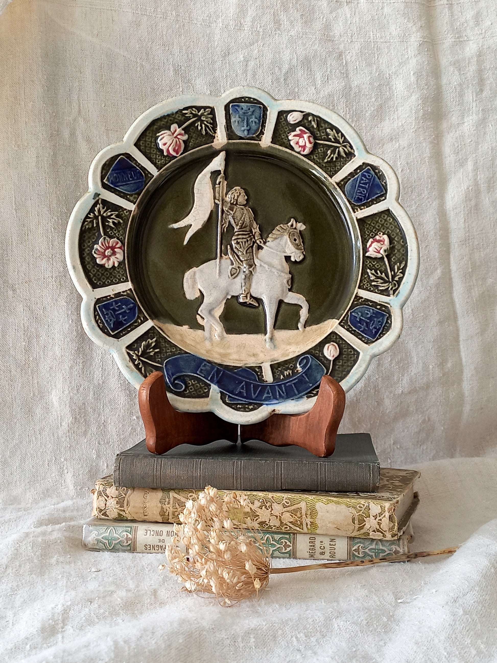 Decorative plate with a scene of Joan of Arc on a horse, surrounded by decorative elements on a white background.