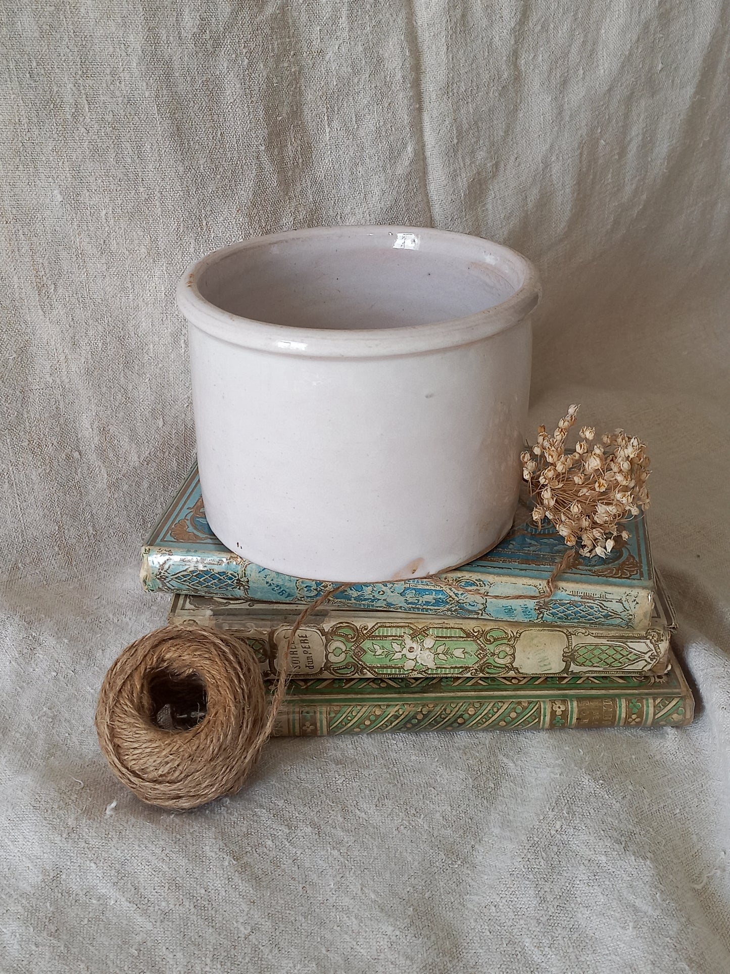 antique jam pot on a textured surface, dried flowers, and books on a textured surface
