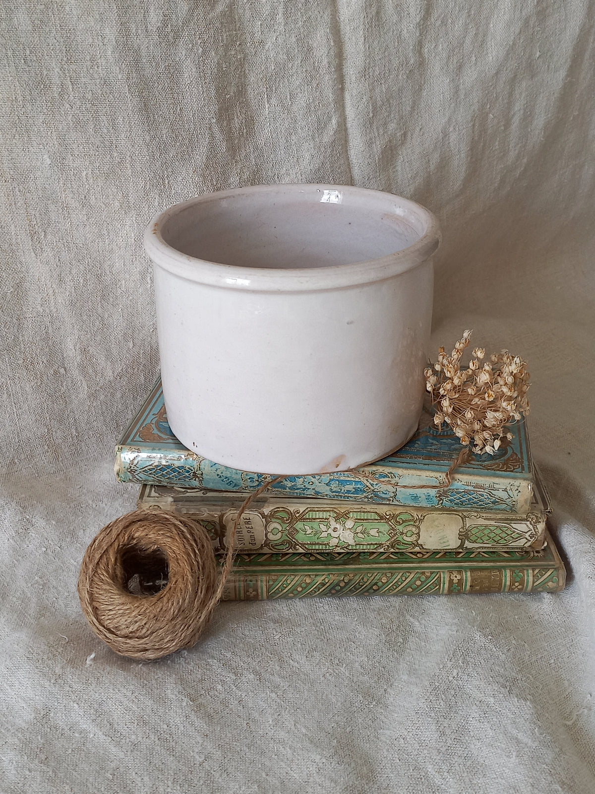 antique jam pot on a textured surface, dried flowers, and books on a textured surface
