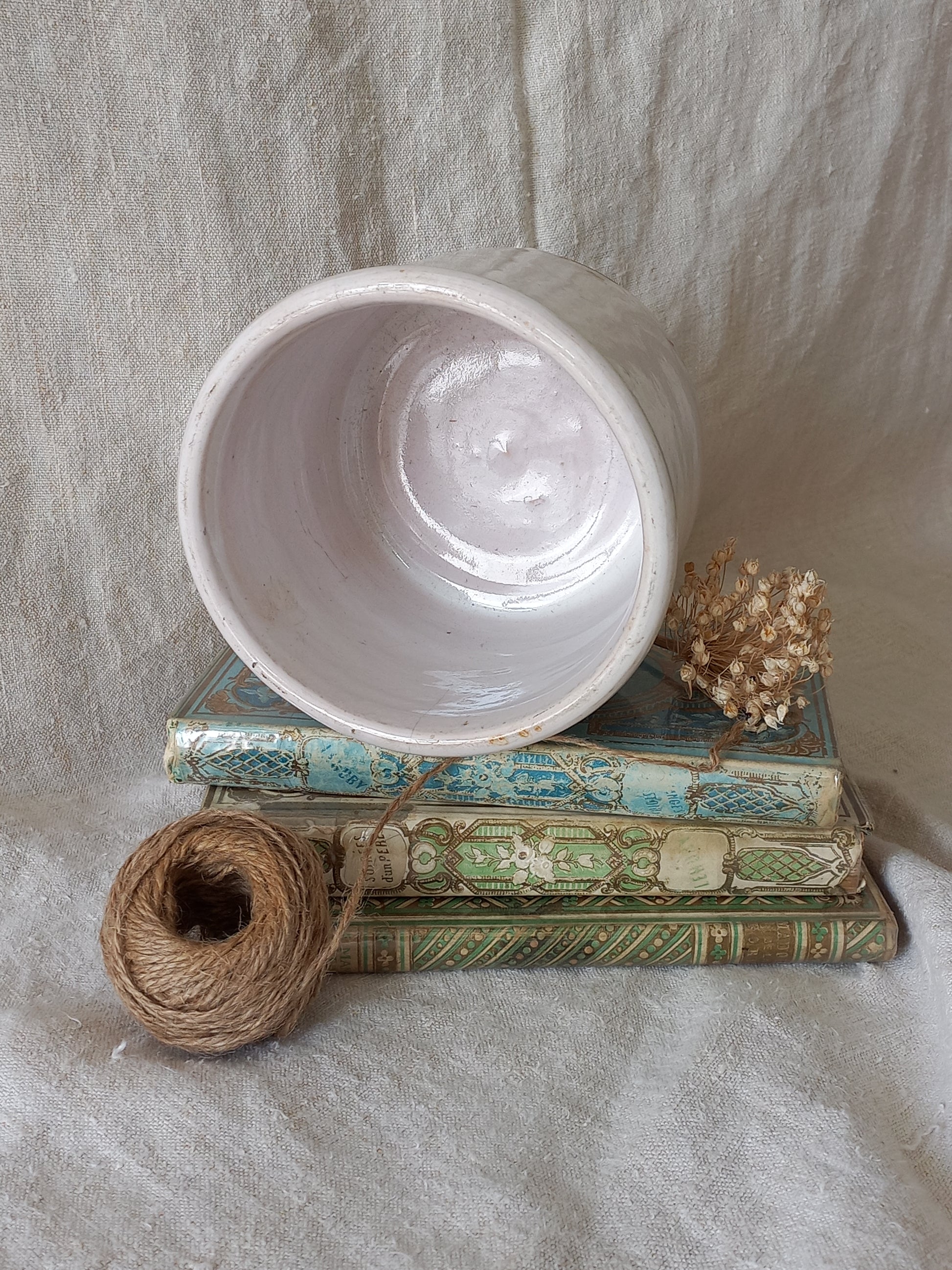 Interior of antique jam pot on a textured surface, dried flowers, and books on a textured surface
