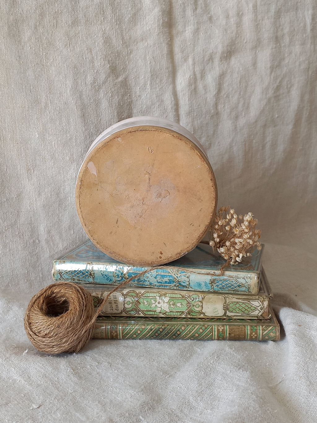 Underneath of antique jam pot on a textured surface, dried flowers, and books on a textured surface