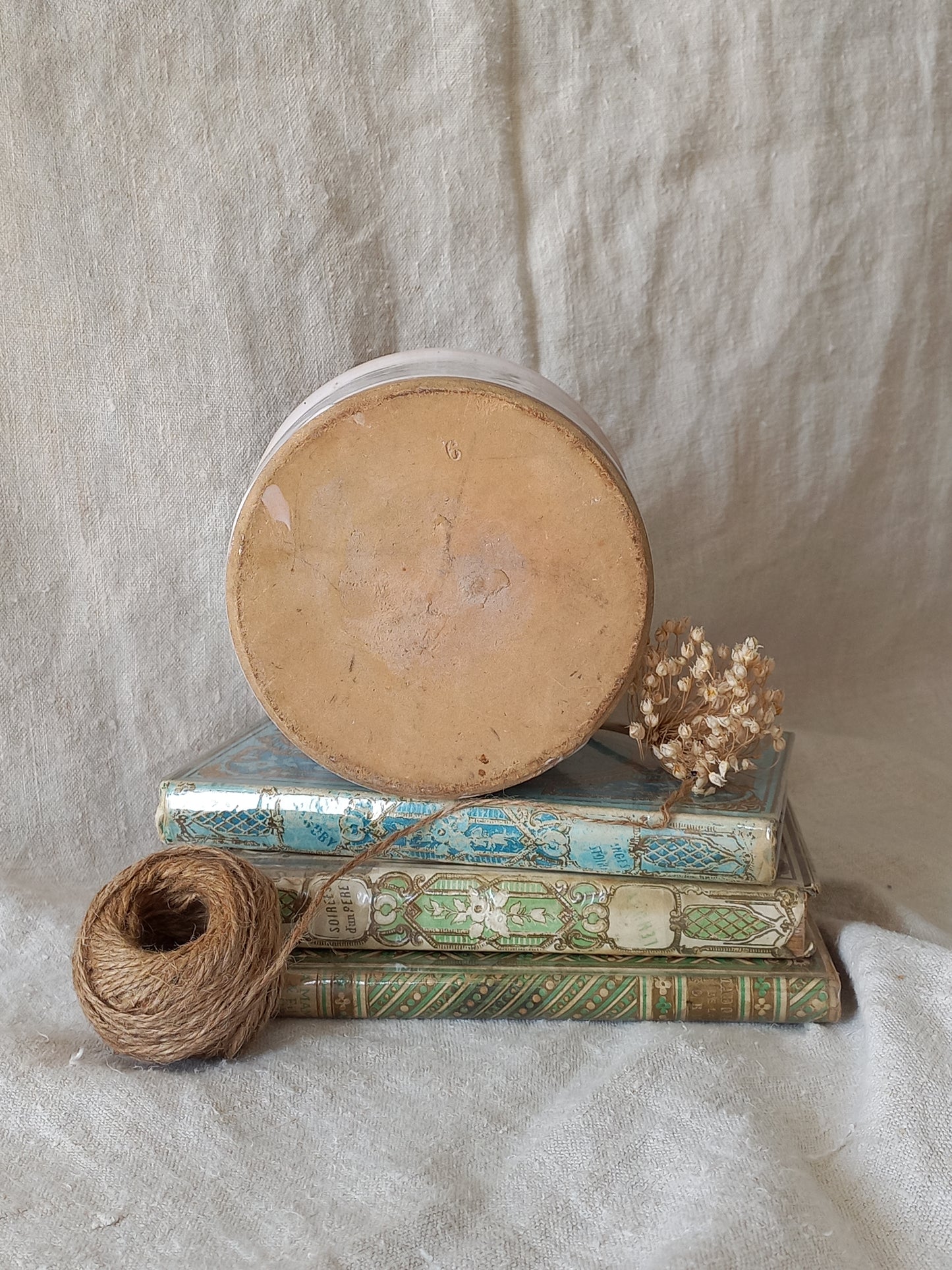 Underneath of antique jam pot on a textured surface, dried flowers, and books on a textured surface