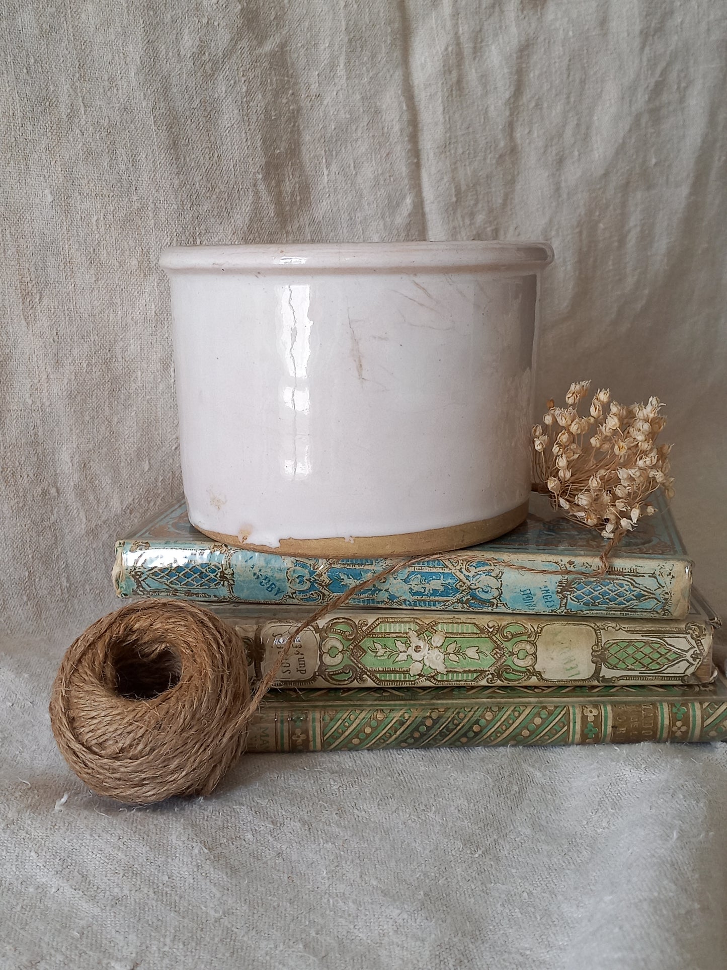 antique jam pot on a textured surface, dried flowers, and books on a textured surface