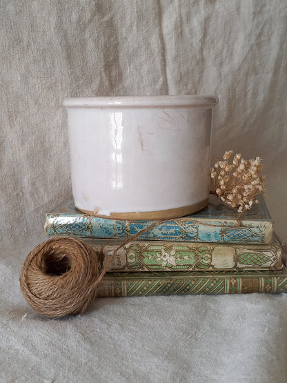 antique jam pot on a textured surface, dried flowers, and books on a textured surface