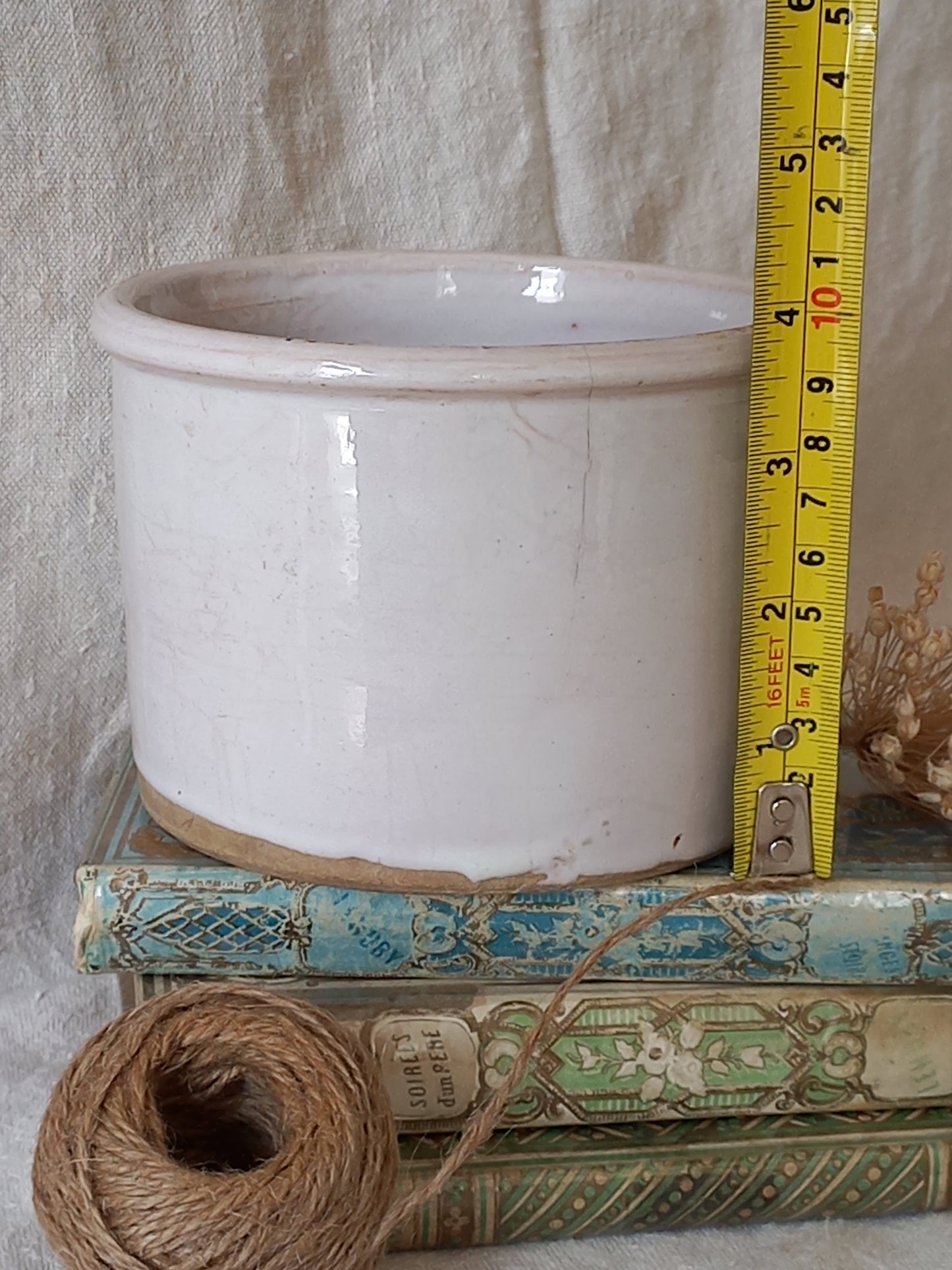 antique jam pot on a textured surface, dried flowers, books on a textured surface and a tape measure for reference.