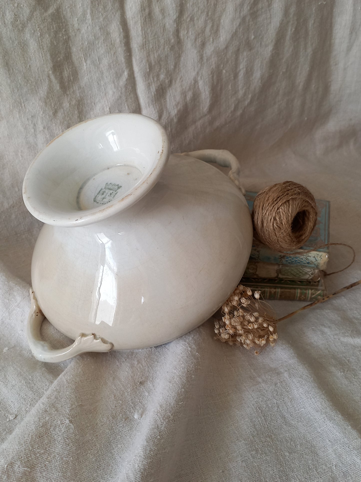 White ironstone bowl on a stack of books with twine and dried flowers against a textured fabric background