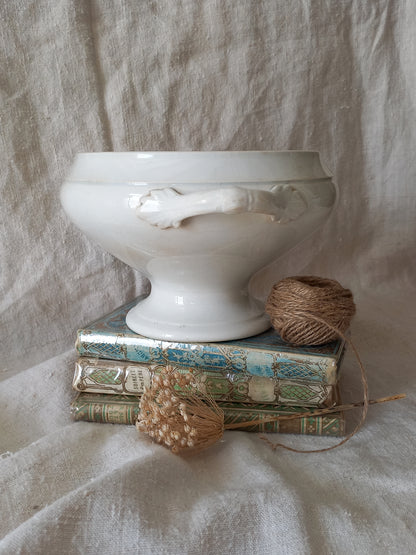 White ironstone bowl on a stack of books with twine and dried flowers against a textured fabric background