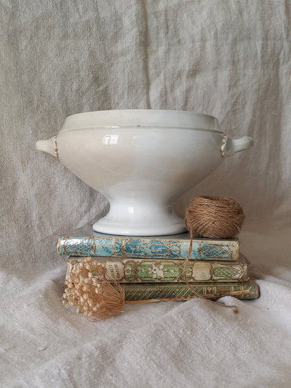 White ironstone bowl on a stack of books with twine and dried flowers against a textured fabric background