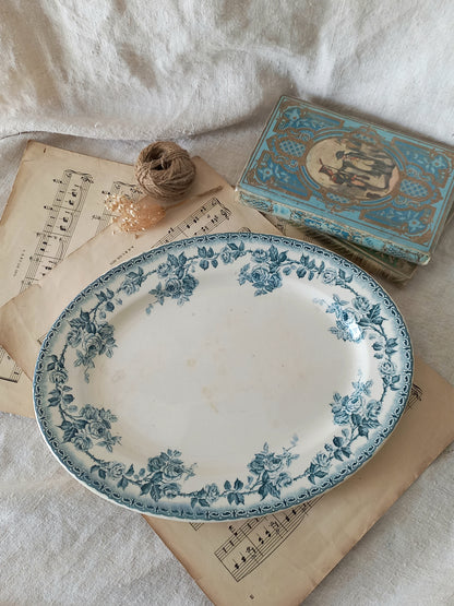 A vintage blue and white floral ceramic serving platter displayed on antique sheet music, next to a small decorative box and twine on a white fabric background.