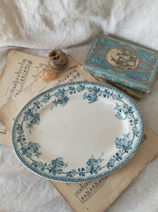 A vintage blue and white floral ceramic serving platter displayed on antique sheet music, next to a small decorative box and twine on a white fabric background.