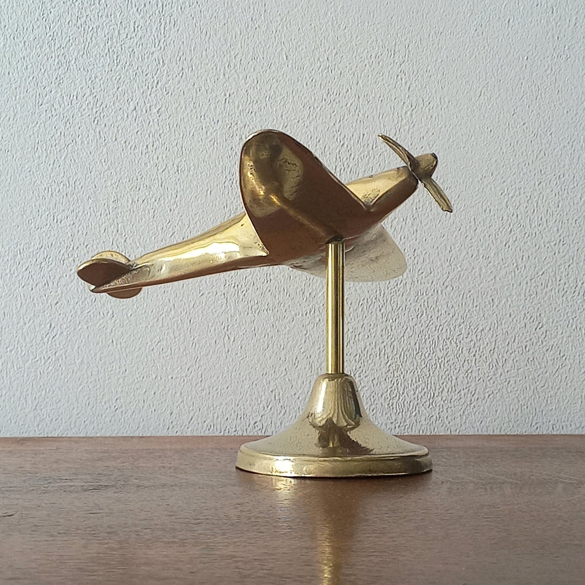 Brass airplane model on a stand against a plain background