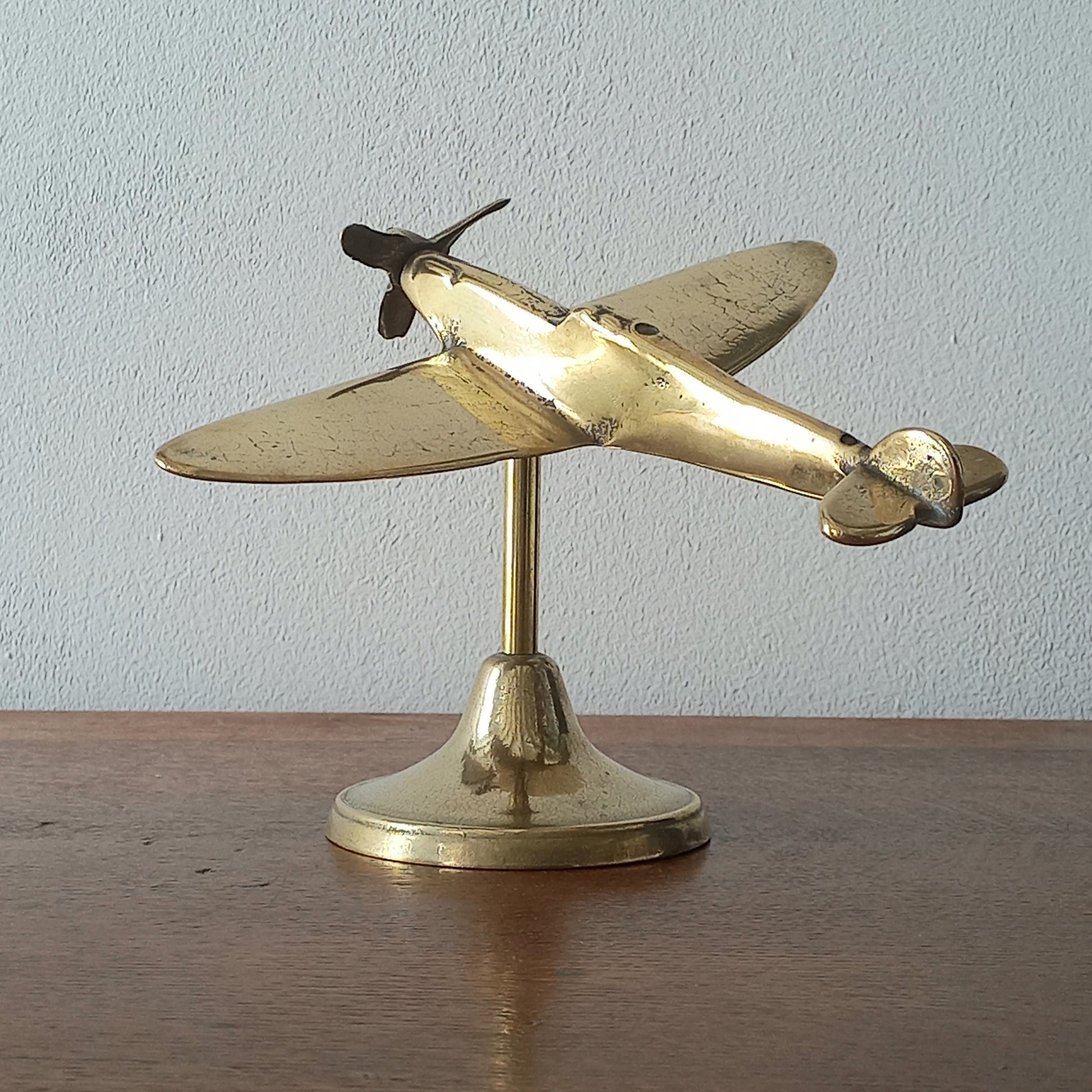 Brass airplane model on a stand against a plain background