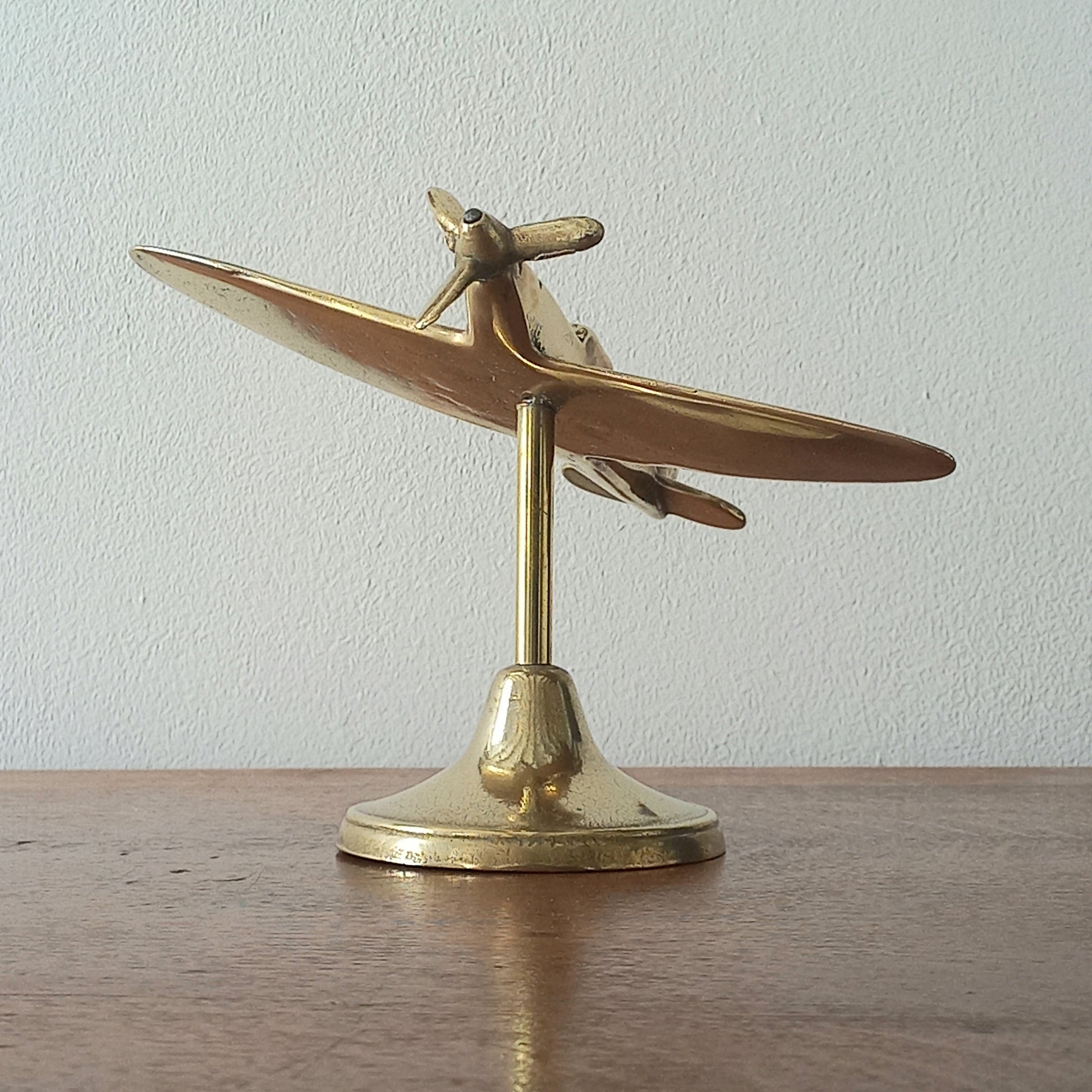 Brass airplane model on a stand against a plain background