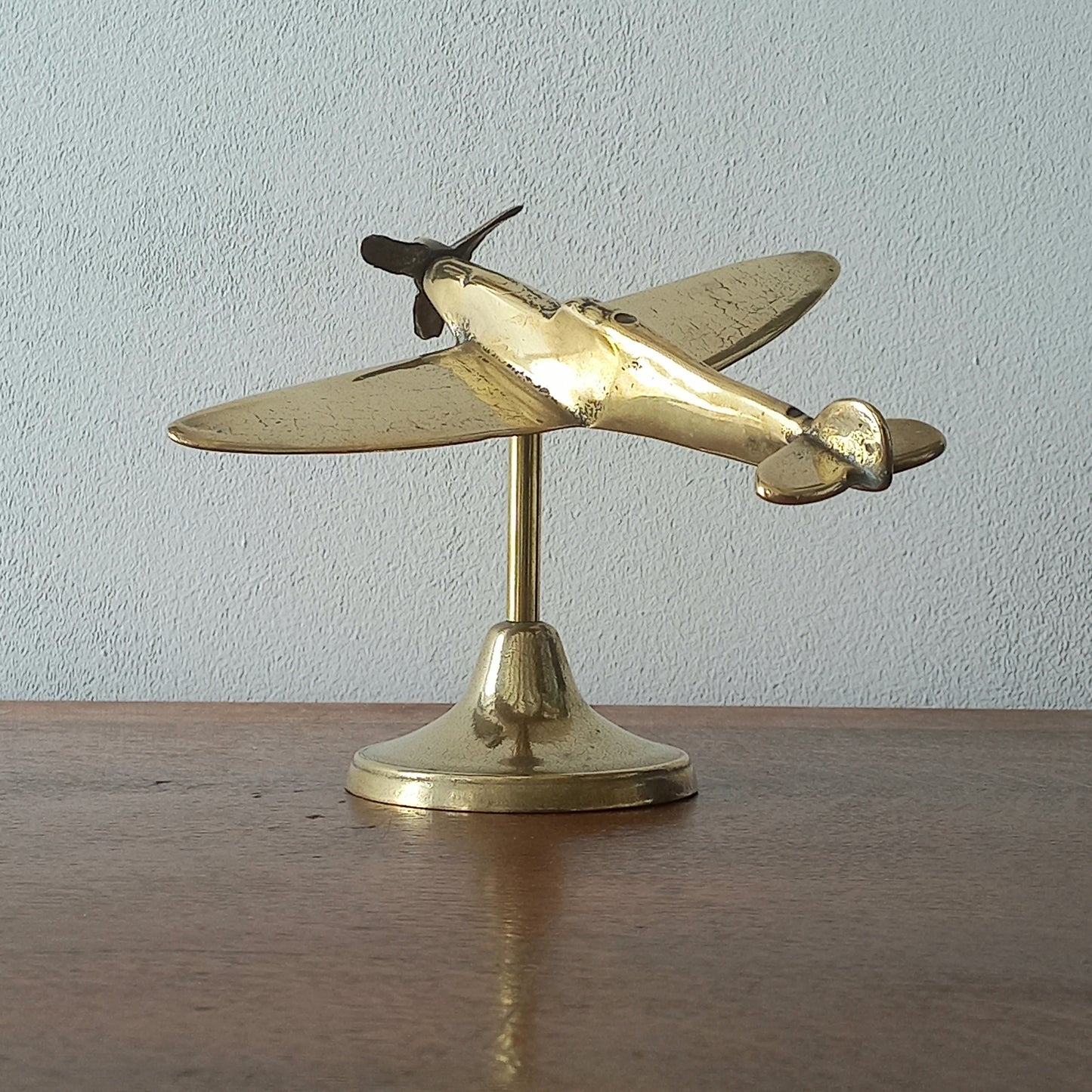 Brass airplane model on a stand against a plain background