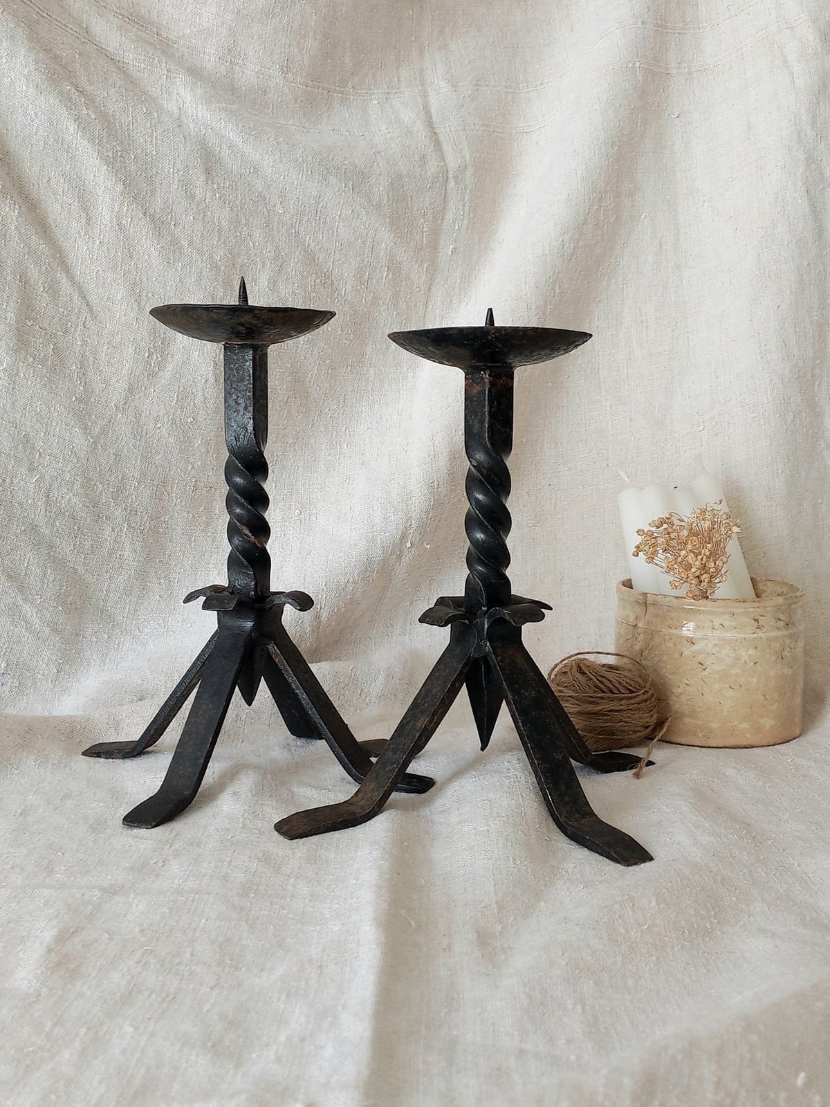 Pair of black wrought iron candle holders on a textured white surface with a woven basket in the background.