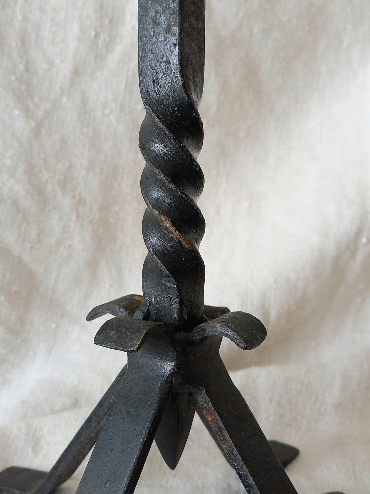 Close-up of a black wrought iron candle holder with a twisted handle on a beige background
