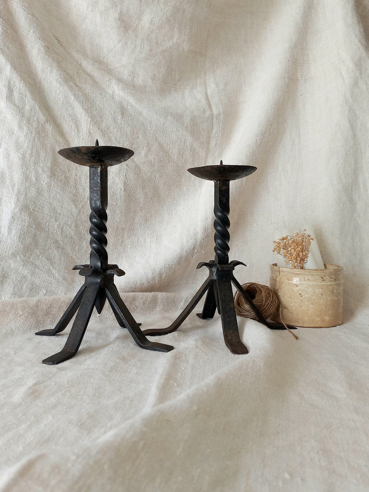 Two black wrought iron candle holders on a white fabric background