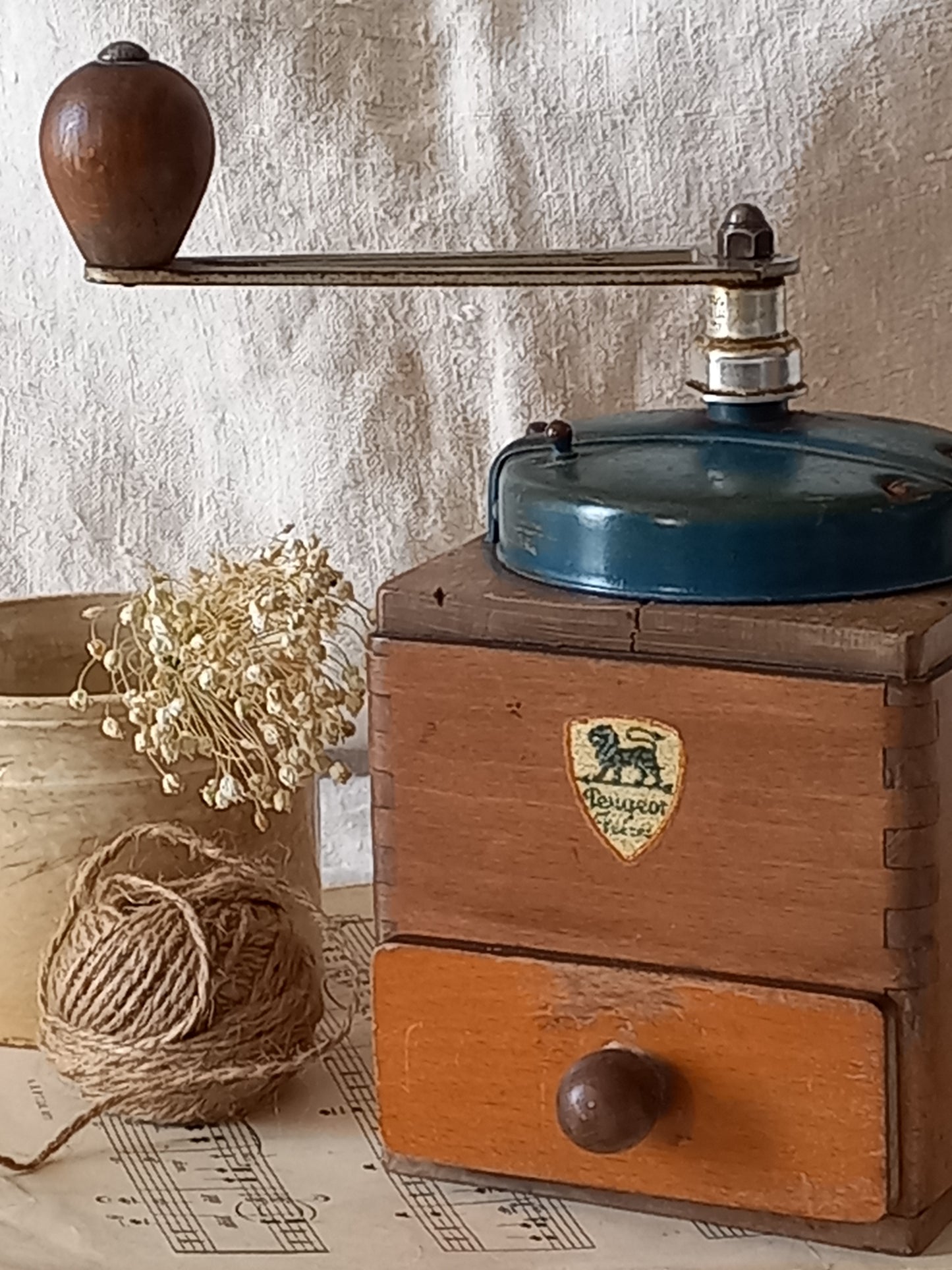 Vintage wooden coffee grinder with a brand logo on a textured surface with string and pins.