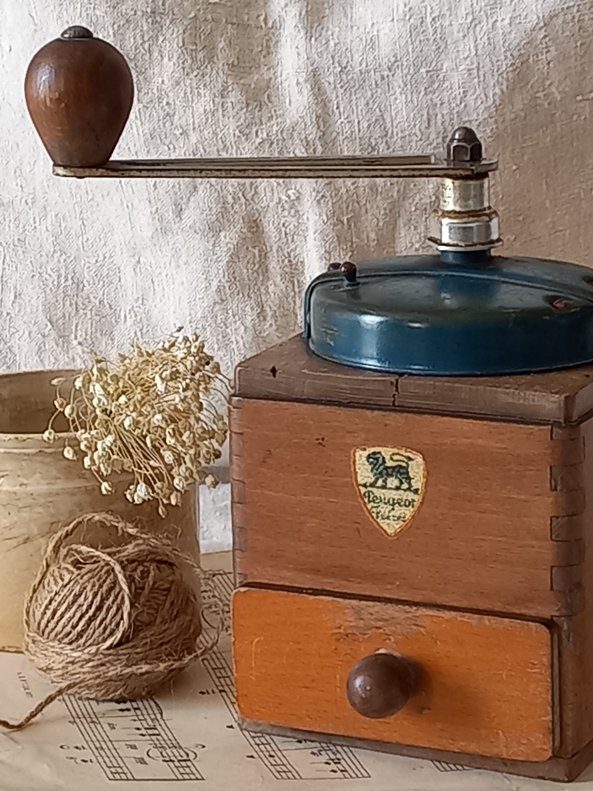 Vintage wooden coffee grinder with a brand logo on a textured surface with string and pins.