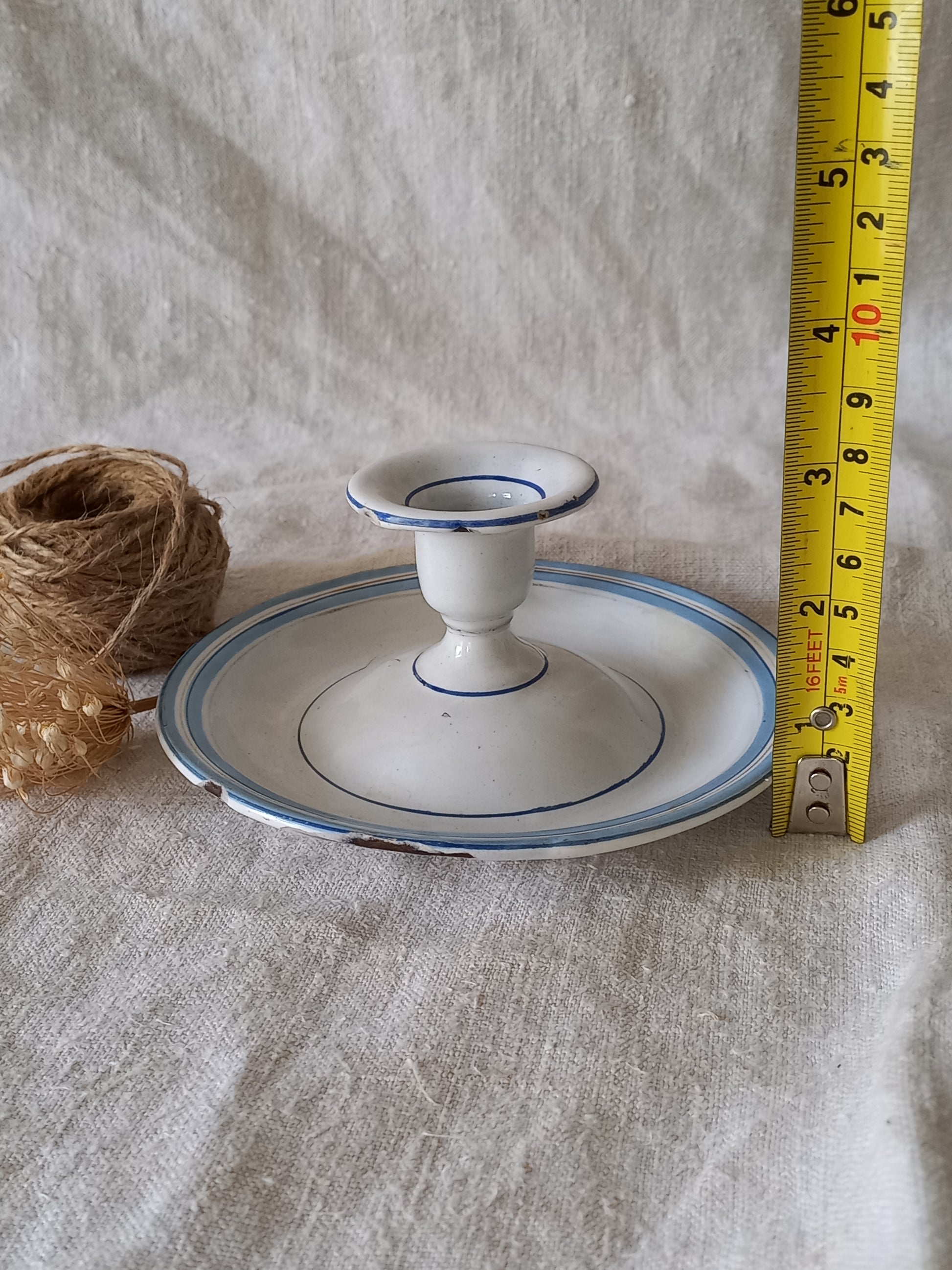 White enamel candle holder with blue rim and measuring tape on a textured surface