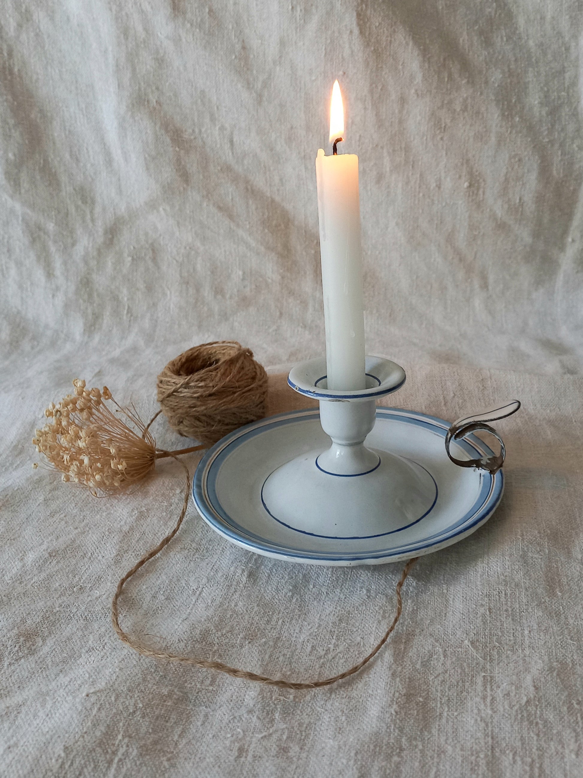 Candle in a white holder on a textured surface with twine and dried flowers.