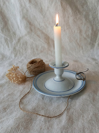 Candle in a white holder on a textured surface with twine and dried flowers.