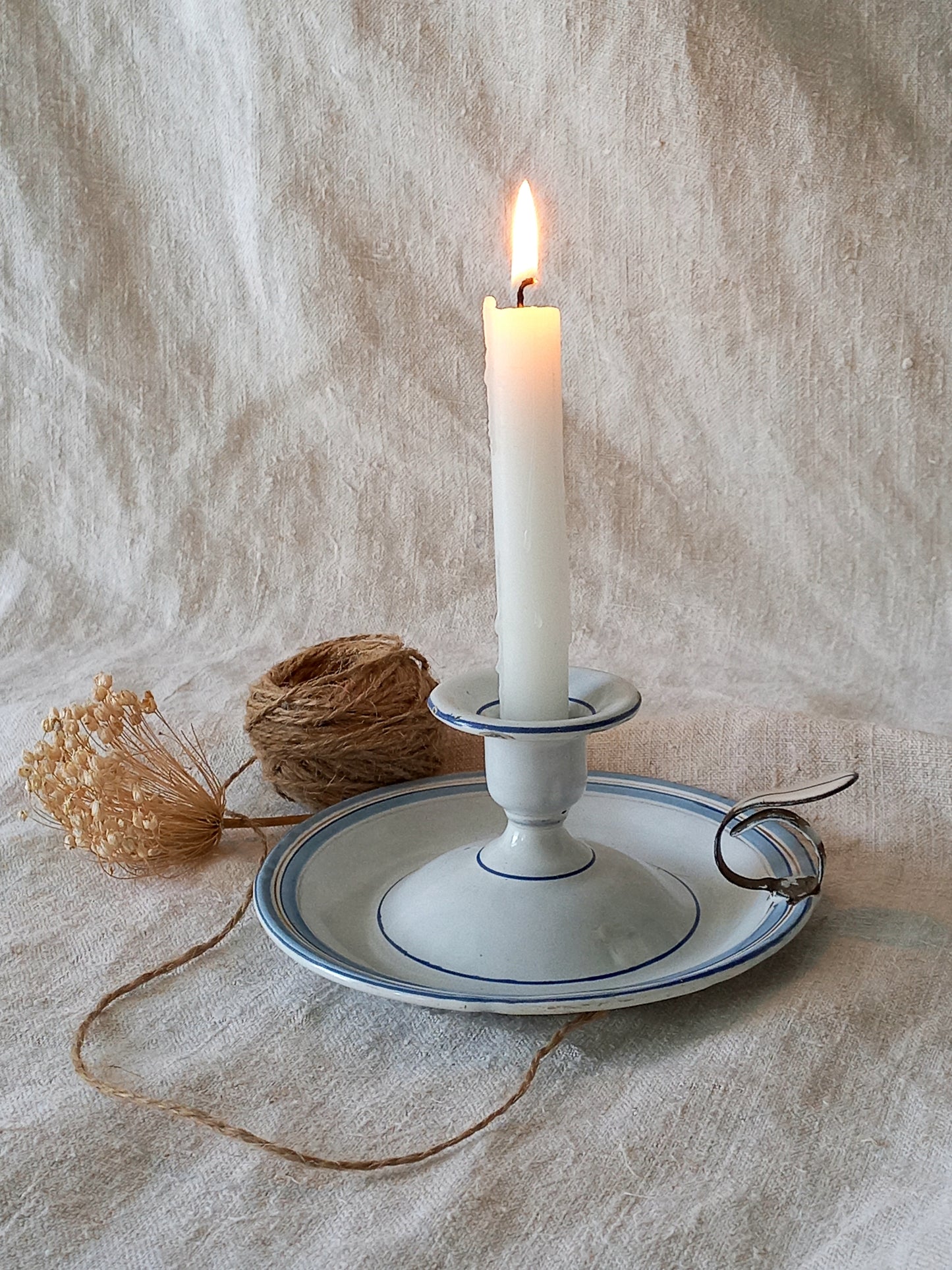 Candle in a white candlestick holder on a textured surface with twine and dried flowers.