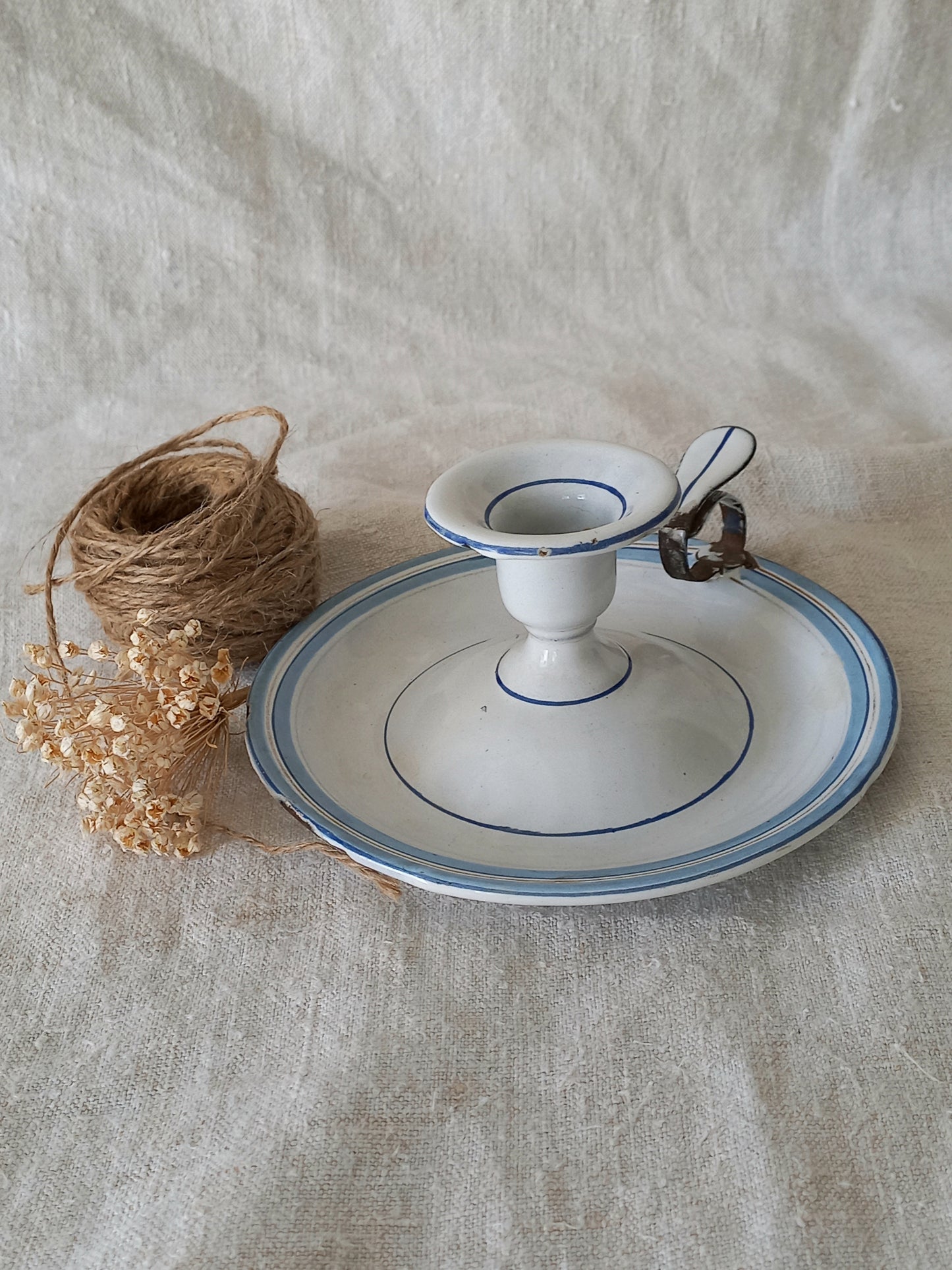 White enamel candle holder with blue rim on a textured beige surface next to twine and dried flowers.