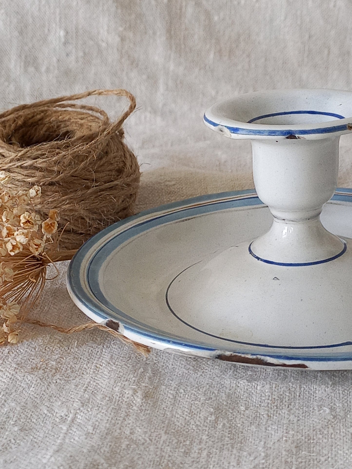 enamel candle holder with blue rim on a textured surface with twine and dried flowers.