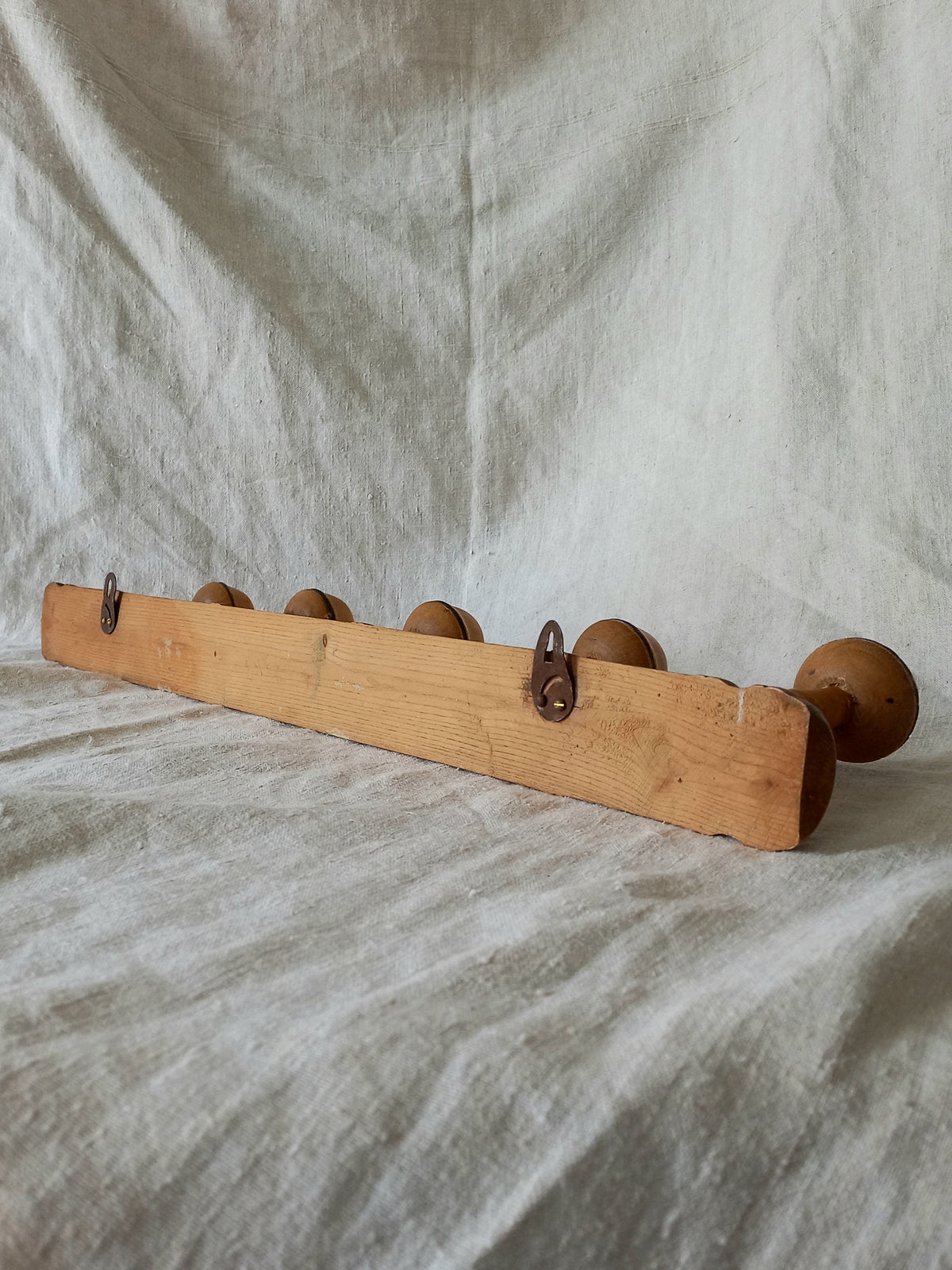 Rear of wooden coat rack with 5 hooks on a textured fabric background