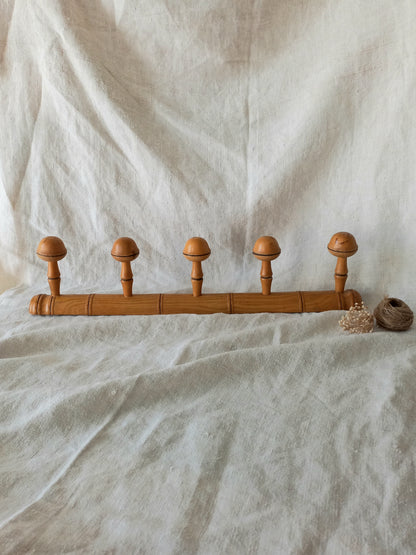 Wooden garment rack with five round wooden pegs on a textured white fabric background
