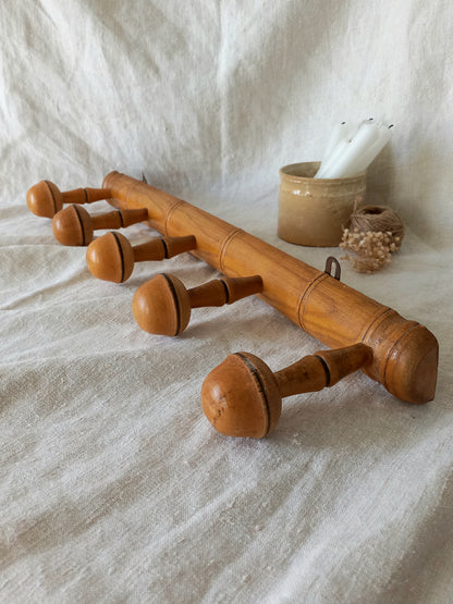Wooden coat rack with acorn-like pegs on a textured fabric background