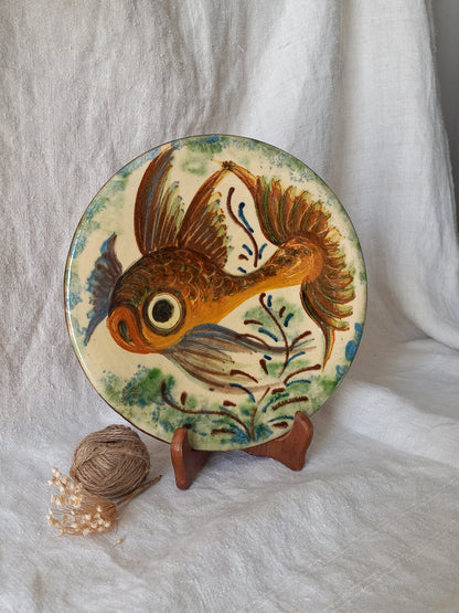 A round ceramic plate with a hand-painted goldfish design, displayed on a small wooden stand against a draped white fabric background.