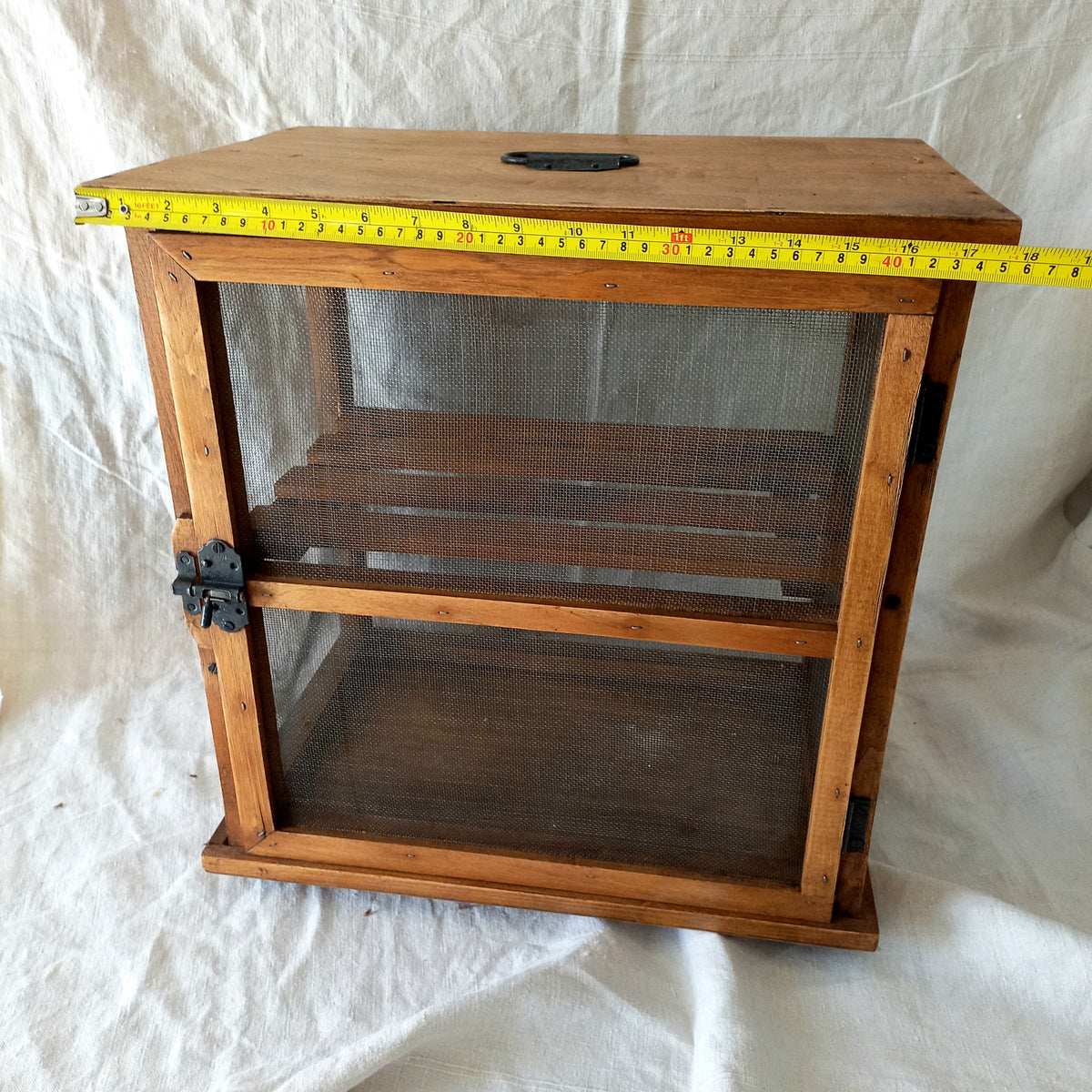 Wooden cabinet with mesh doors on a white background, measured with a tape measure.