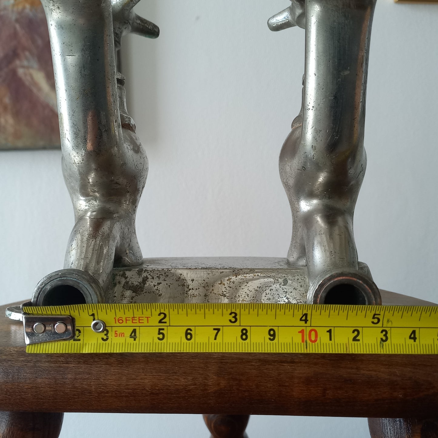 Close-up of a vintage metal faucet on a wooden background  with a measuring tape showing its dimensions against a plain background