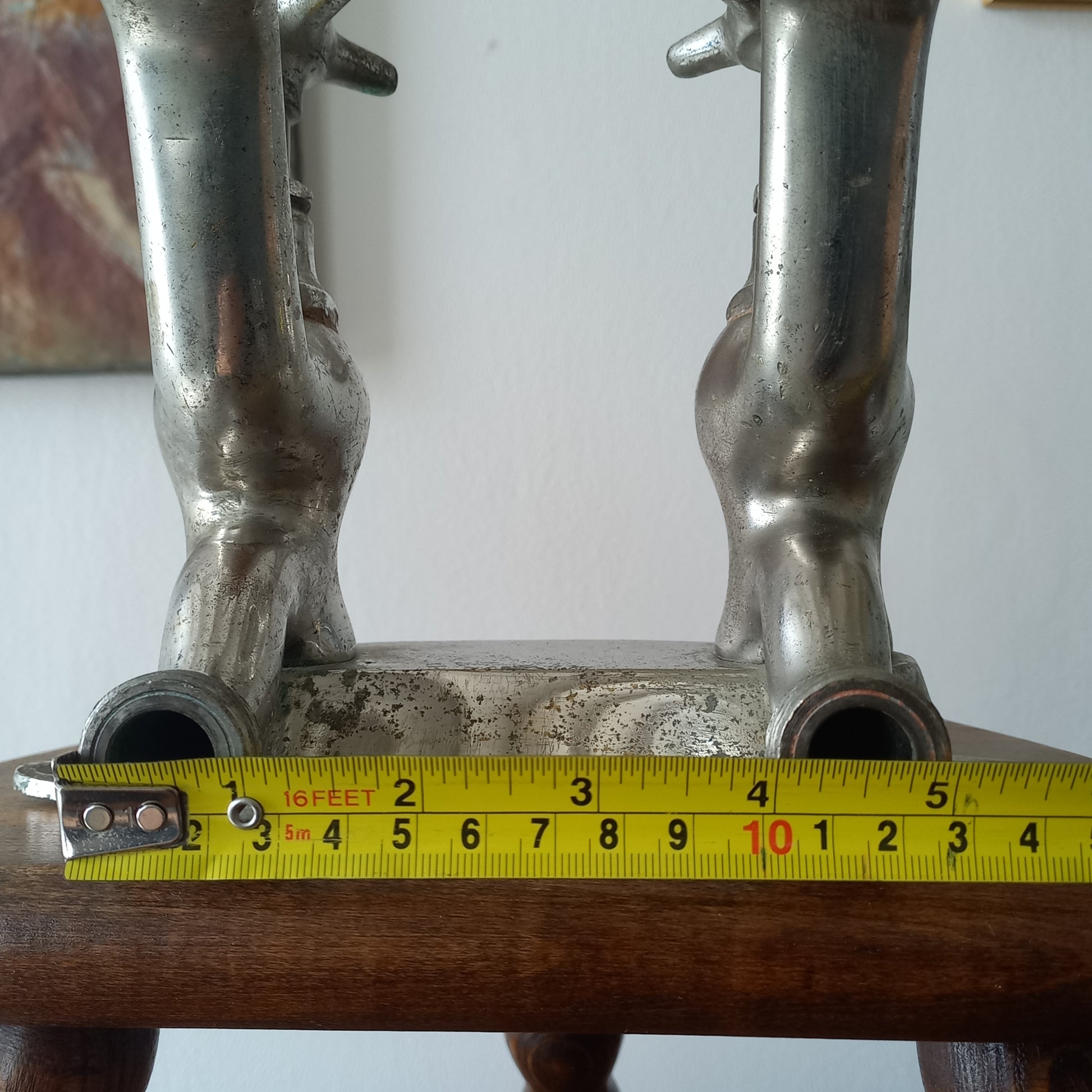 Close-up of a vintage metal faucet on a wooden background  with a measuring tape showing its dimensions against a plain background