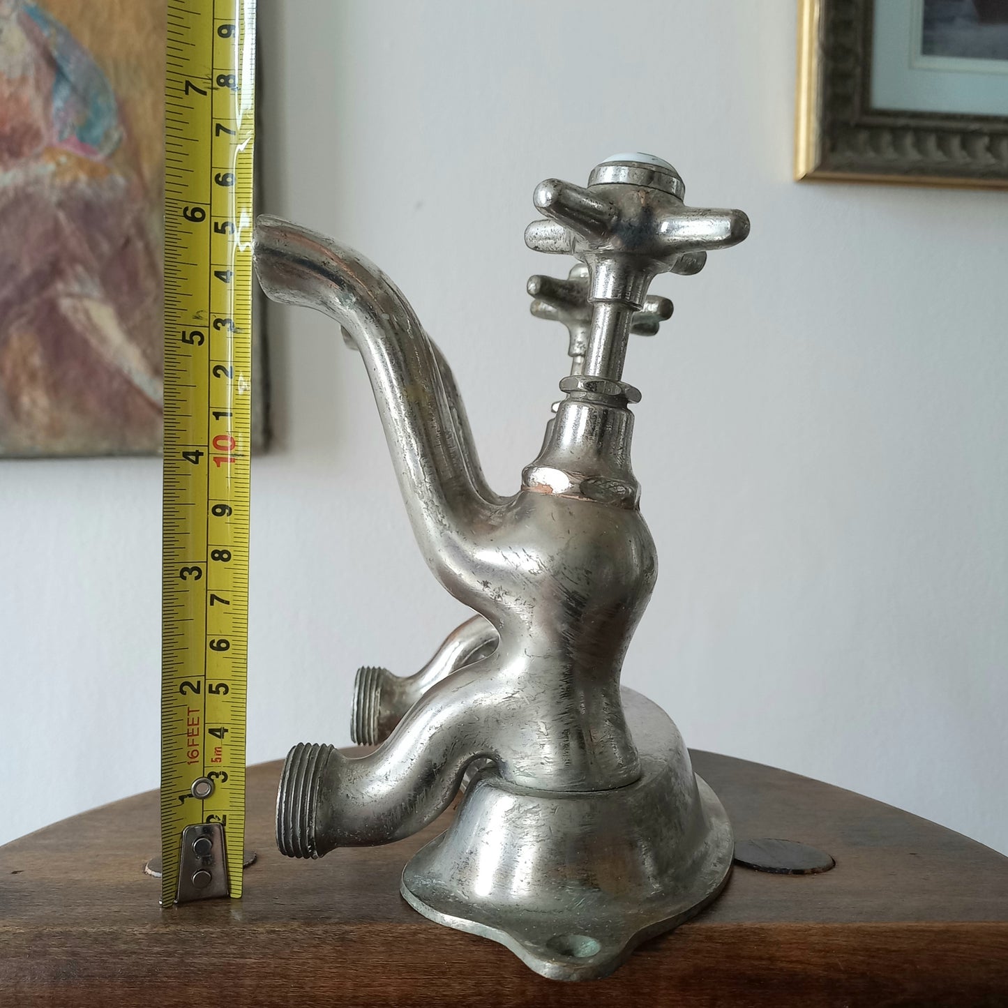 Close-up of a vintage metal faucet on a wooden background  with a measuring tape showing its dimensions against a plain background