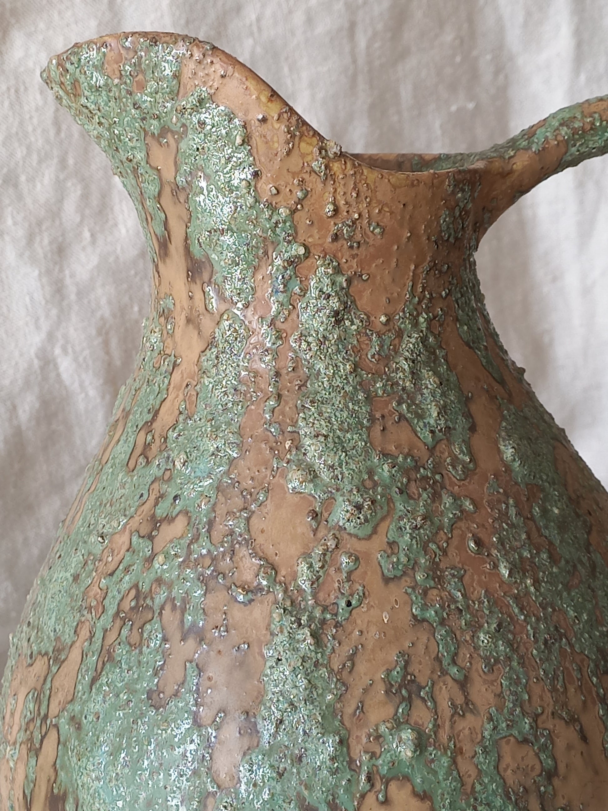 Close-up of large artisan made vintage pottery jug with green and earth tones on a beige background