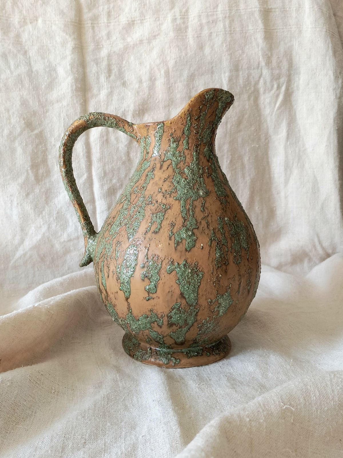 Large artisan made vintage pottery jug with green and earth tones on a beige background