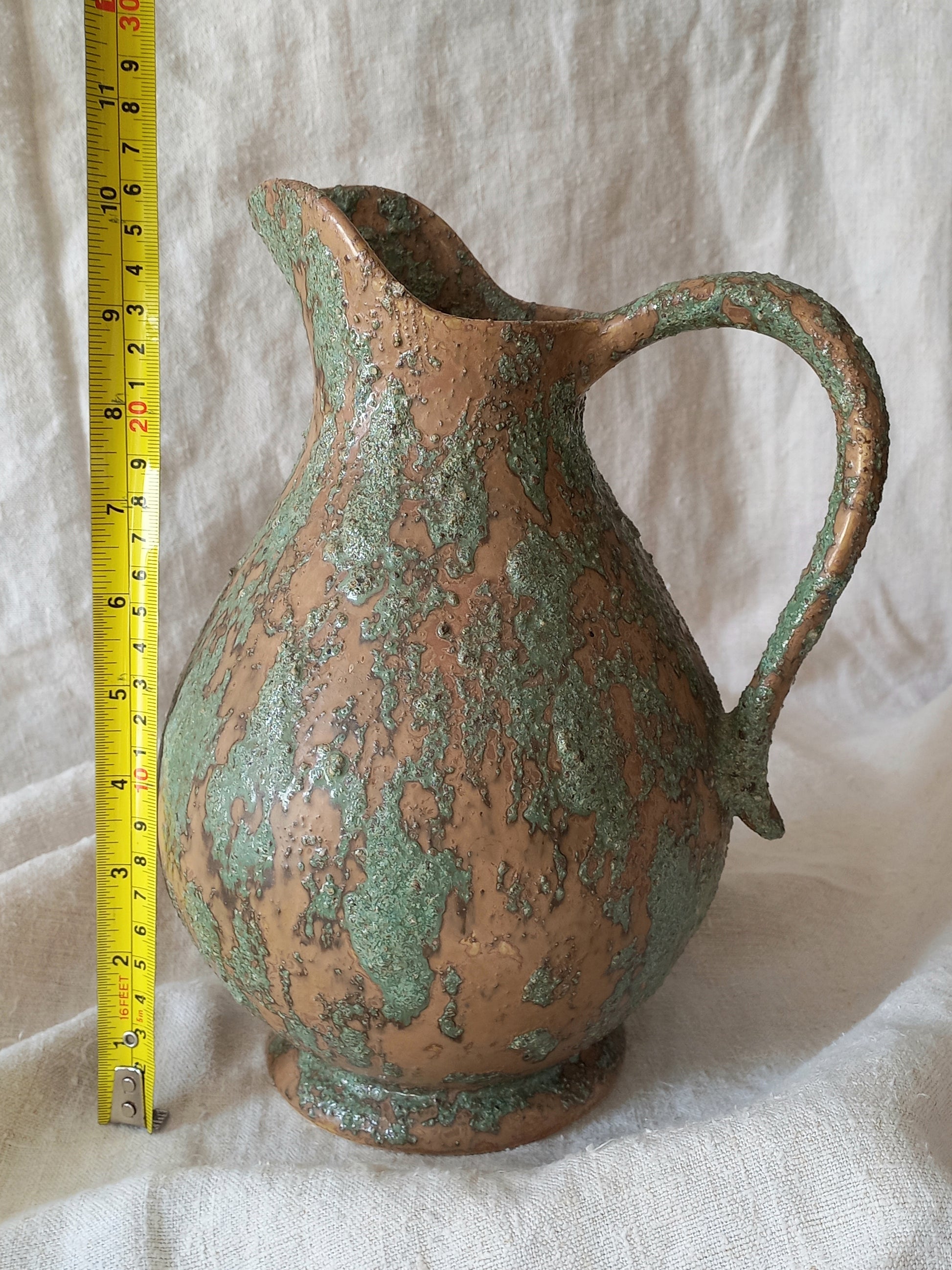 Large artisan made vintage pottery jug with green and earth tones on a beige background