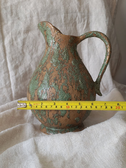 Large artisan made vintage pottery jug with green and earth tones on a beige background